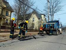 Public Works staff fix pothole on the road with maintenance truck in the distance